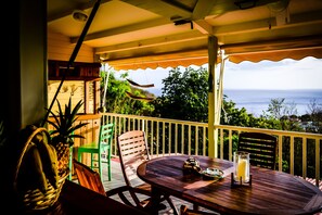 A wooden table with chairs on a balcony overlooking a scenic view. - Harmonie Tropicale (Bouillante)