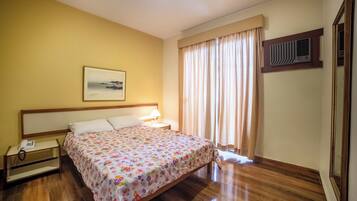 Quarto bem arrumado com uma cama, abajur e telefone num criado-mudo.