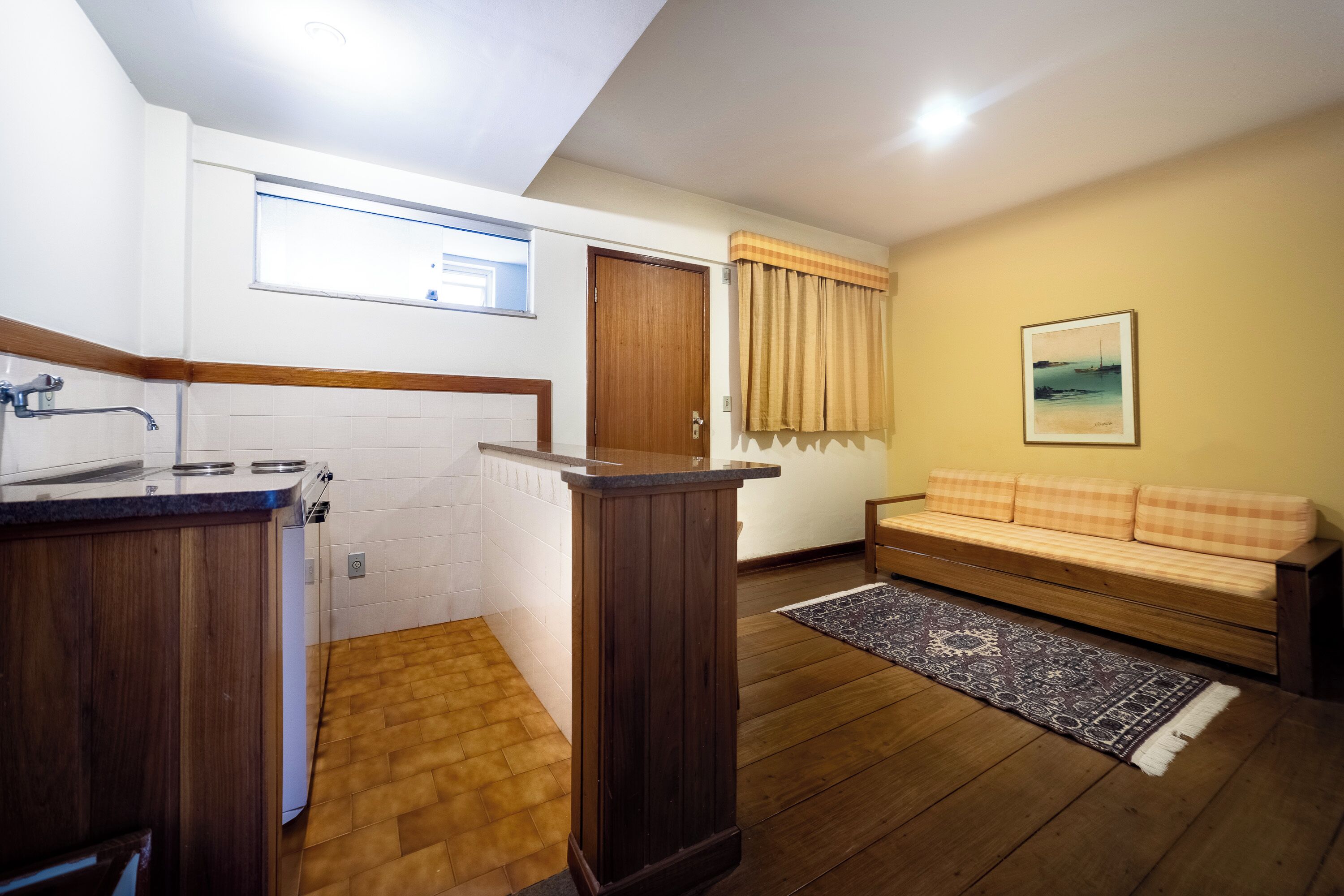 Un espacio habitable compacto con kitchenette, piso de madera, sofá y alfombra.