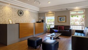 Un área de recepción moderna con un escritorio de madera, otomanas de cuero negro, un sofá y una mesa de centro.