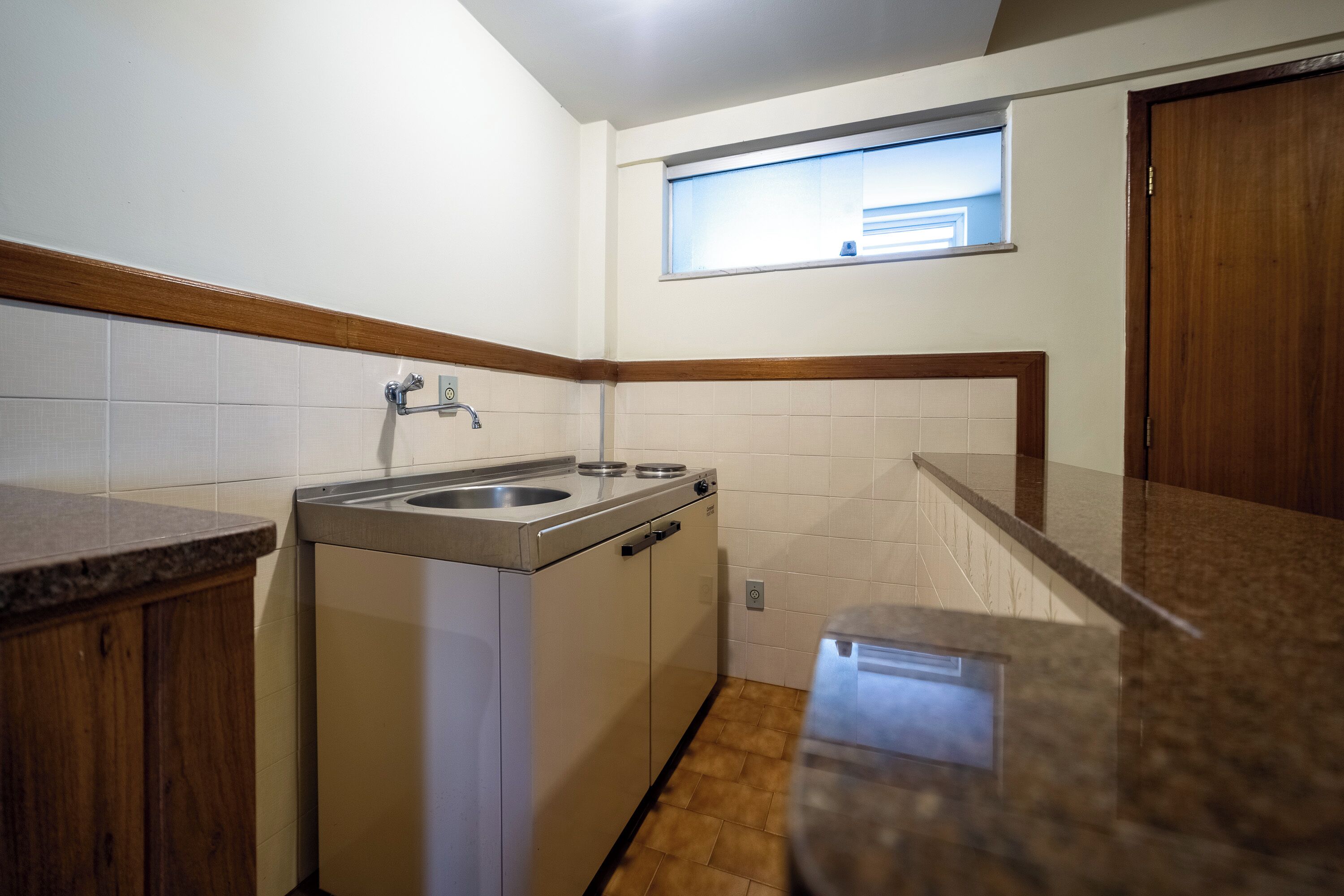 A compact kitchen with a sink, countertop, and wooden cabinets.