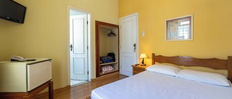 Un dormitorio con cama, mesita de noche, lámpara, armario y televisor sobre un mueble.