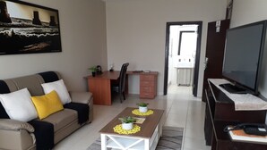 A living room with a sofa, coffee table, TV, and a dining area with a desk and chair. - Prost Hotel (Swakopmund)