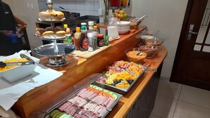 A buffet counter with various food items, condiments, and a beverage dispenser. - Prost Hotel (Swakopmund)