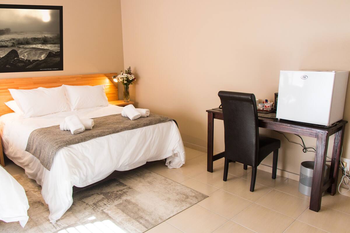 A hotel room with a bed, a desk, a chair, a refrigerator, and a trash can.