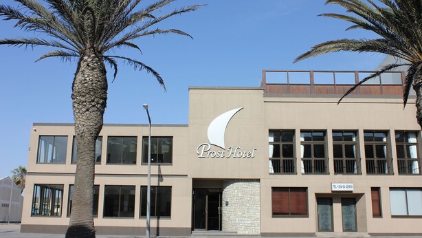 A modern hotel with a prominent crescent moon logo, large windows, and a brick facade. - Prost Hotel (Swakopmund)