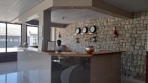 A reception desk at Prost Hotel with a stone wall backdrop, clocks, and a framed certificate. - Prost Hotel (Swakopmund)