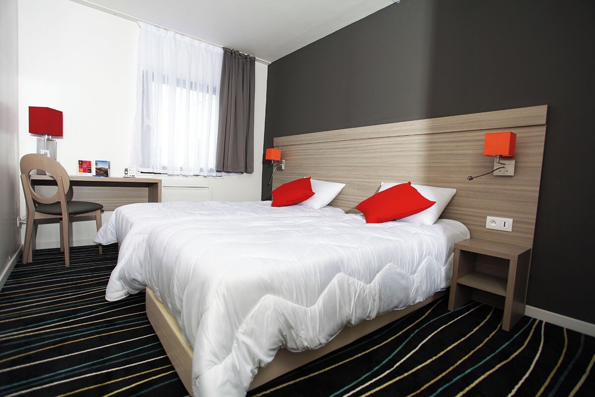 Une chambre d’hôtel avec un lit, un bureau, une chaise et une fenêtre avec des rideaux.