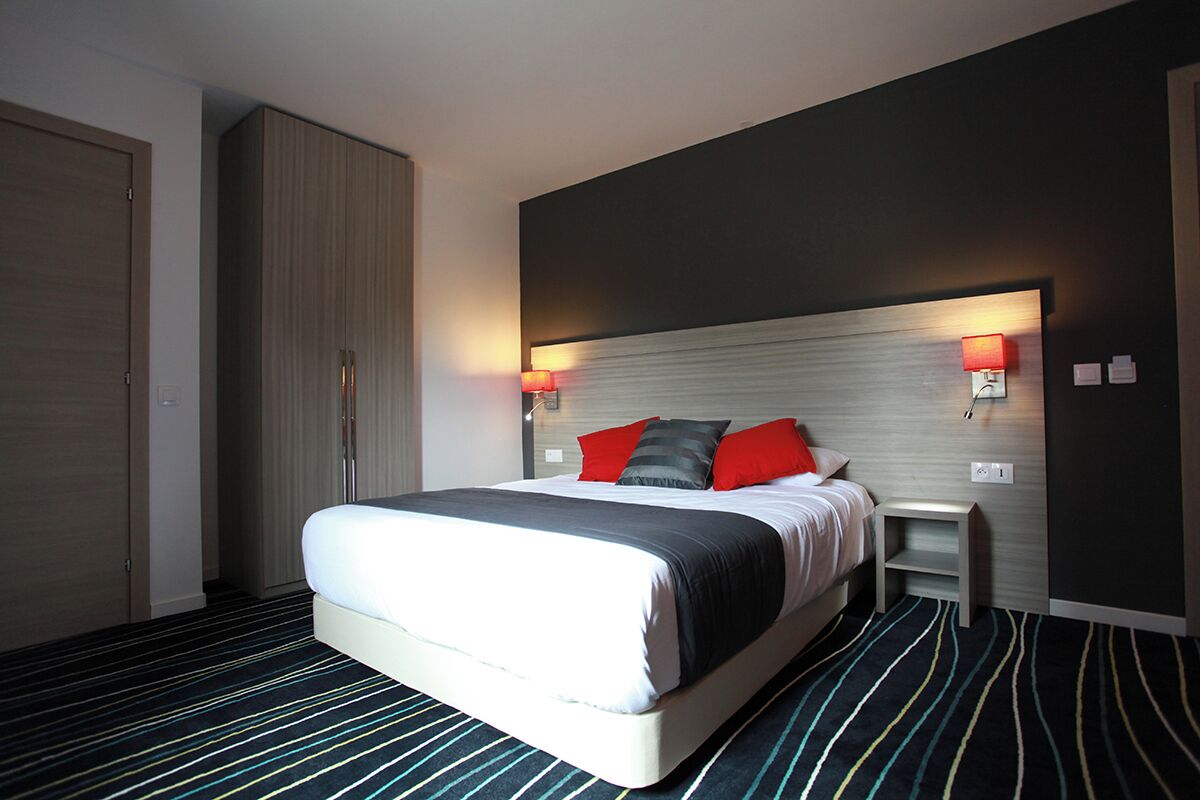 Une chambre d’hôtel avec un lit, des lampes de chevet, une armoire et un sol recouvert de moquette.