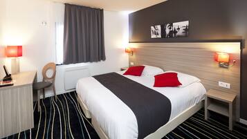 A hotel room with a bed, a desk, a chair, a window with curtains, and wall-mounted lamps.