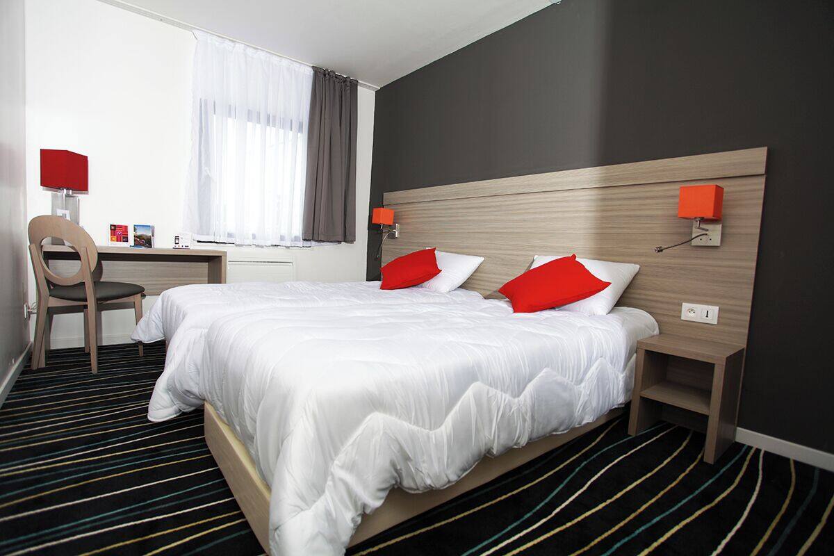 Une chambre d’hôtel avec un lit, un bureau, une chaise et une fenêtre avec des rideaux.