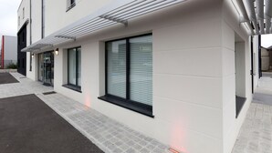 Een modern gebouw met grote ramen, een overdekte gang en een geplaveid entreegebied.