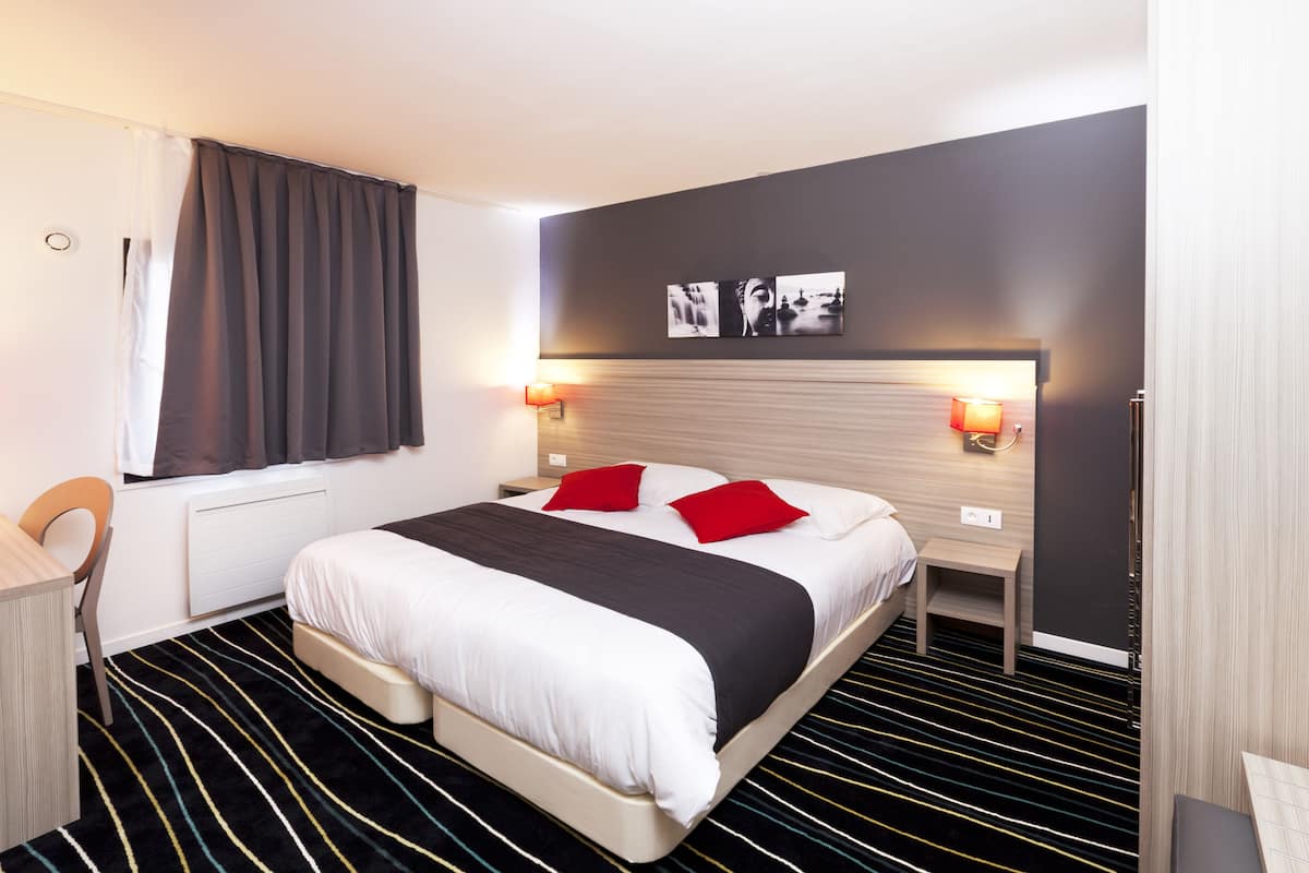 Une chambre d’hôtel moderne avec un grand lit, deux tables de chevet avec des lampes, un bureau et une chaise.