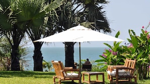 A serene outdoor seating area with two wooden chairs and a table under a white umbrella, overlooking a body of water. - Leo's Beach Hotel & Restaurant - Adults Only (Brufut)
