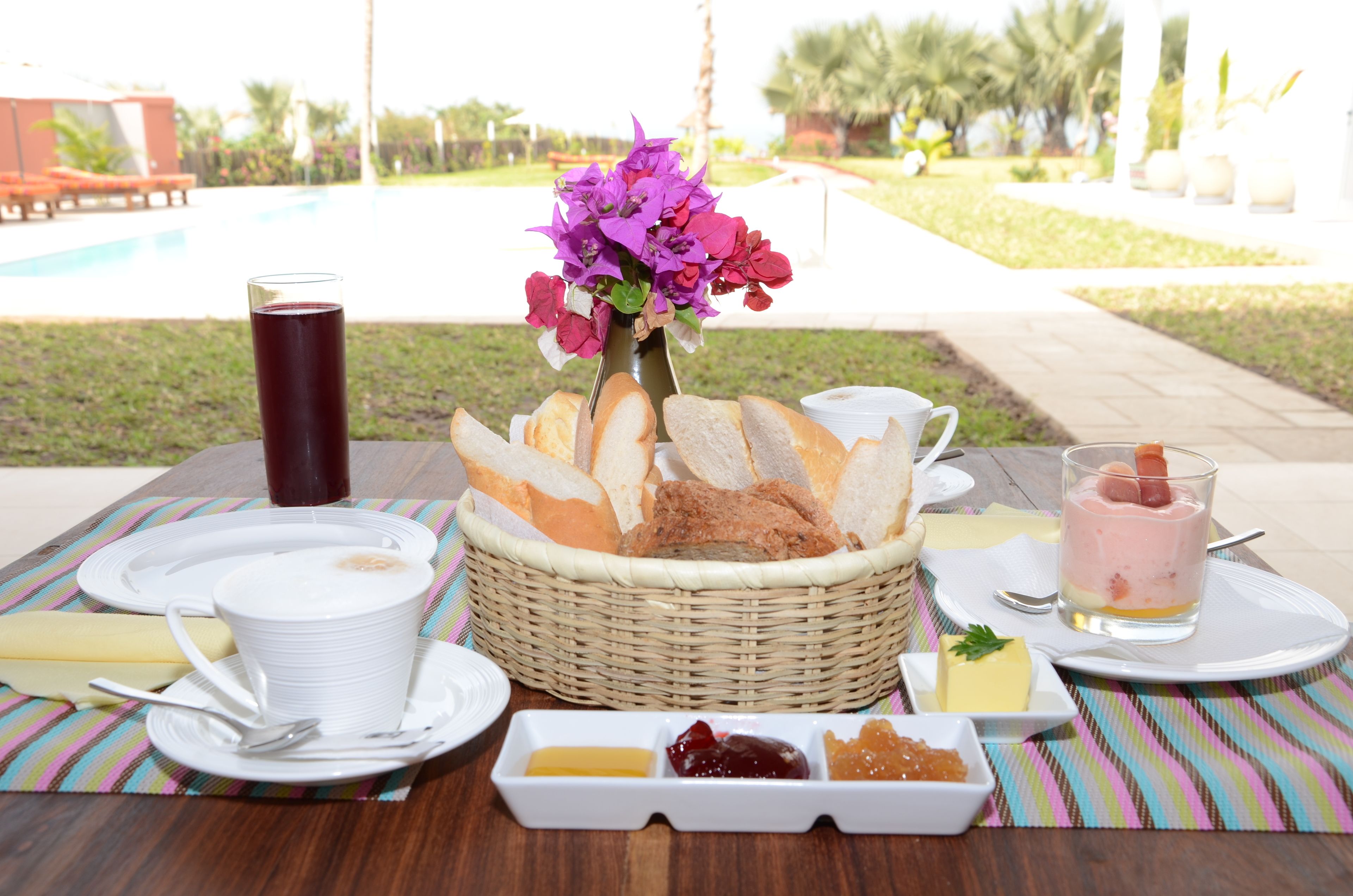 A table set with white plates, a glass of red beverage, a basket of bread, and a dessert with a fruit garnish.