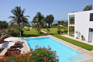 Una piscina con sillas de descanso, palmeras y vista al océano.