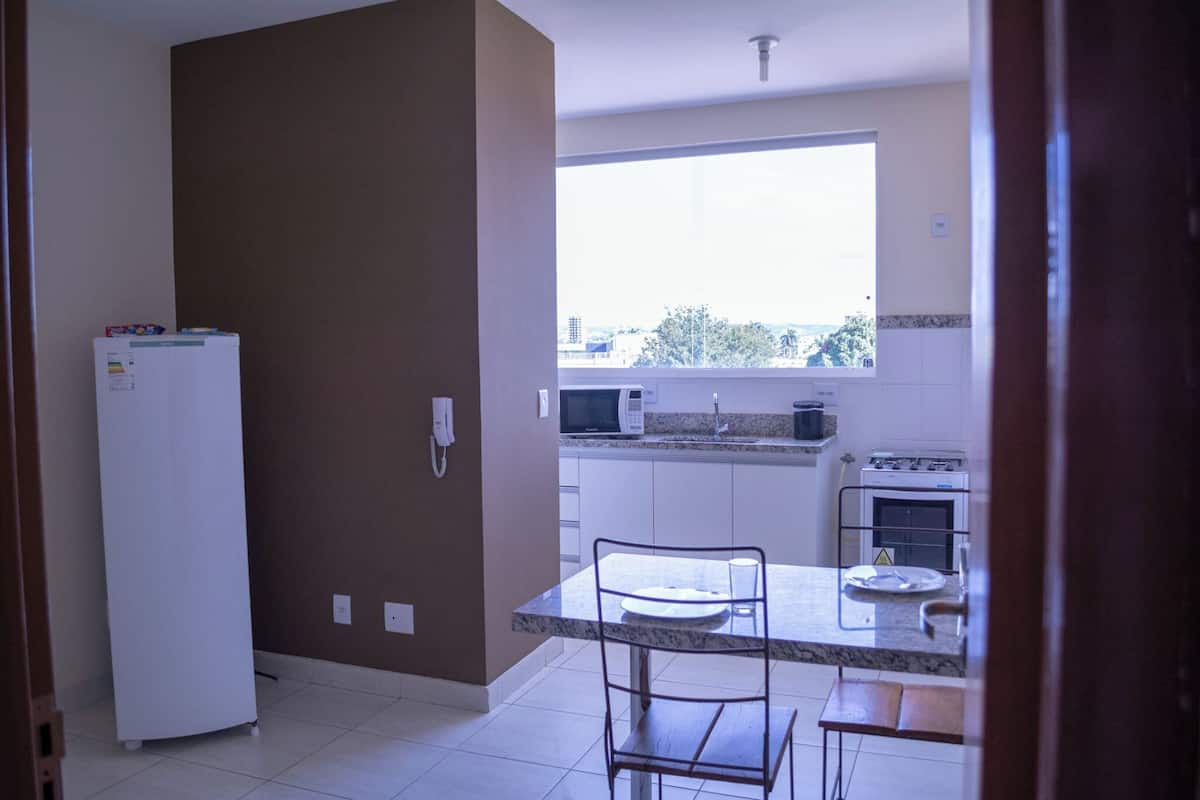 A kitchen with a refrigerator, microwave, stove, and a window with a city view.