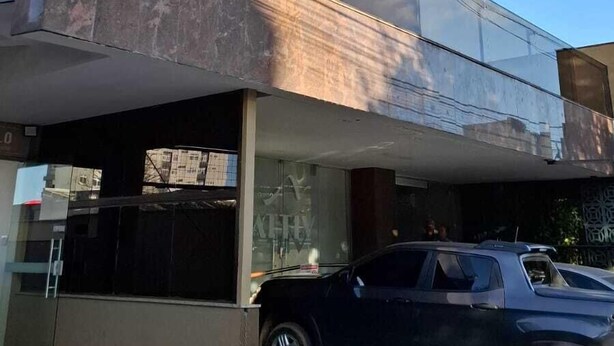 Un edificio moderno de varios pisos con balcones, un coche estacionado adelante y un cielo despejado.