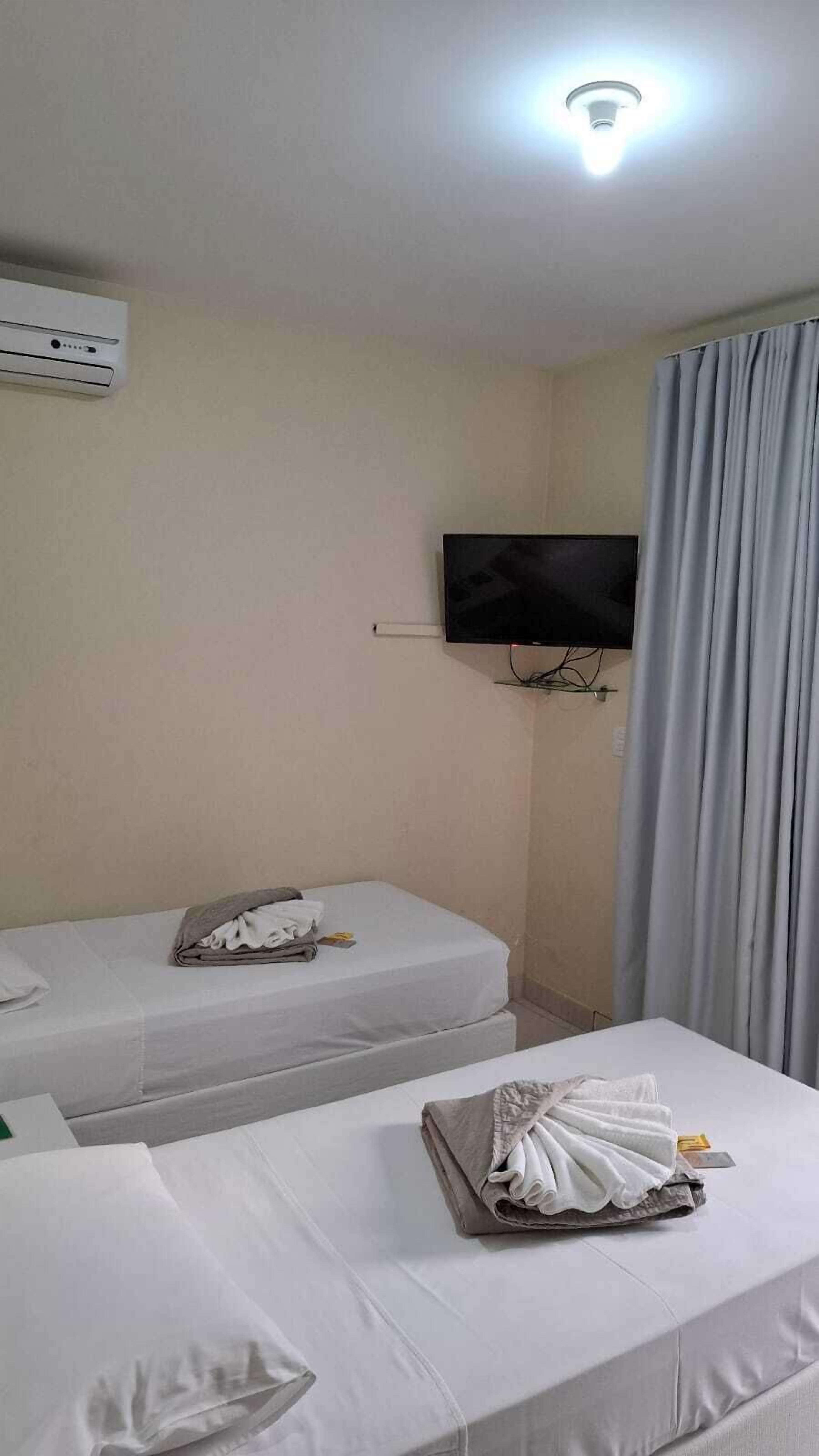 A hotel room with two beds, a TV mounted on the wall, and an air conditioning unit.