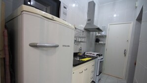 Una cuina compacta amb un frigorífic blanc, una placa de cocció i un microones. Hi ha un rentapeus petit i un armari amb un microones a sobre.