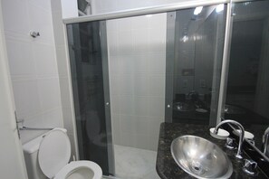 Un baño con inodoro, cabina de ducha de vidrio y lavamanos con espejo.