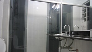 Un bany amb dutxa tancada per vidre, un vàter blanc i un lavabo amb un mirall a sobre.