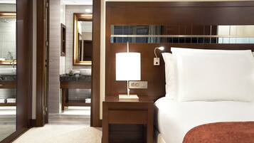 A hotel room with a bed, a nightstand with a lamp, a mirror, and a bathroom with a sink and mirror.