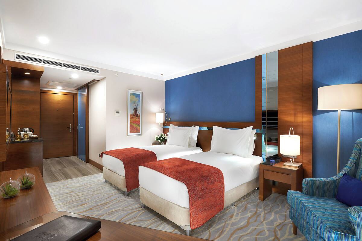 A hotel room with two beds, a desk, a chair, and a nightstand.