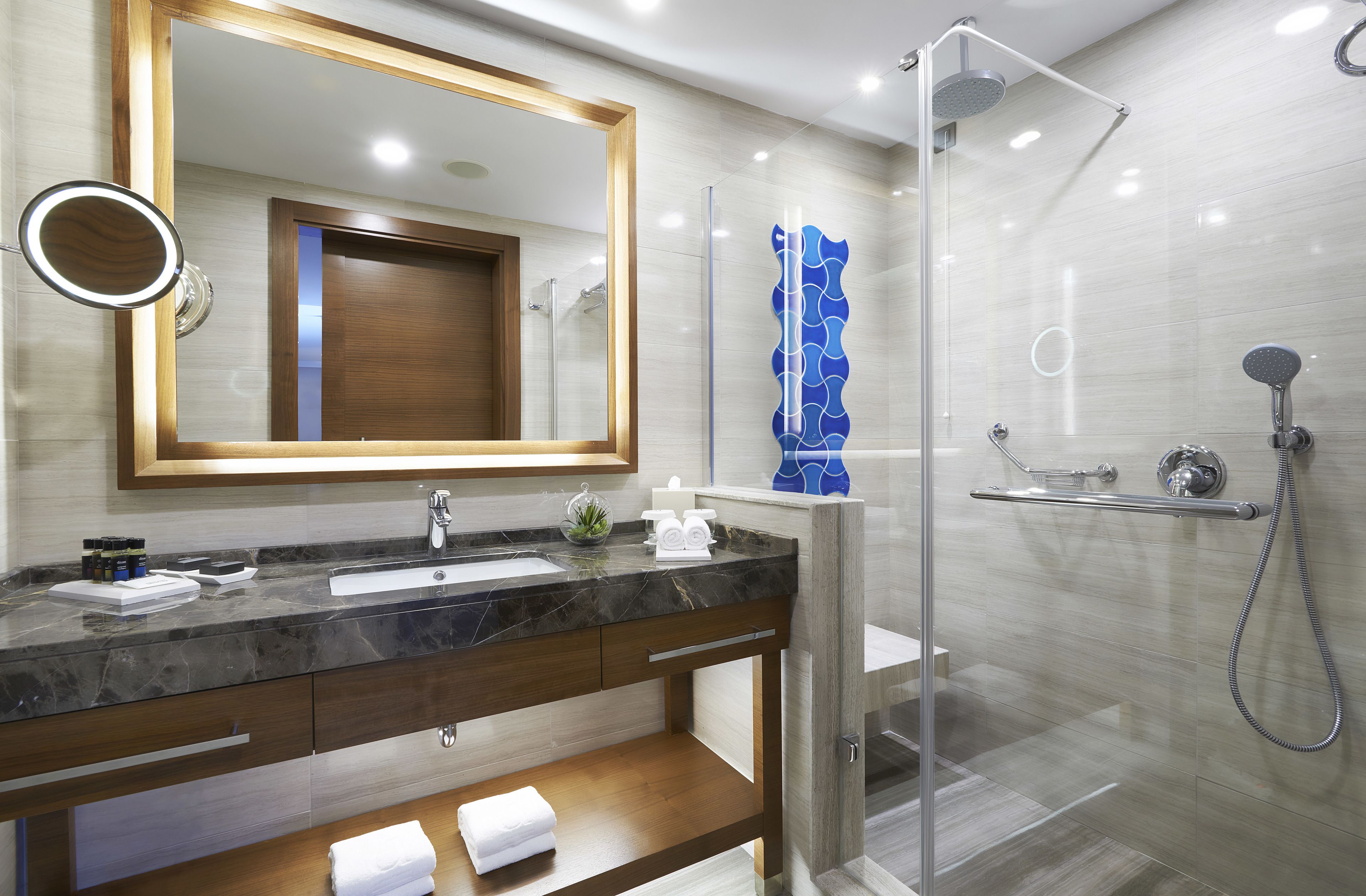 A modern bathroom with a marble sink, a large mirror, a glass shower enclosure, and a wooden vanity.