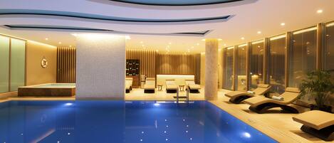 Un área de piscina interior moderna con sillones de descanso y un mostrador de recepción.