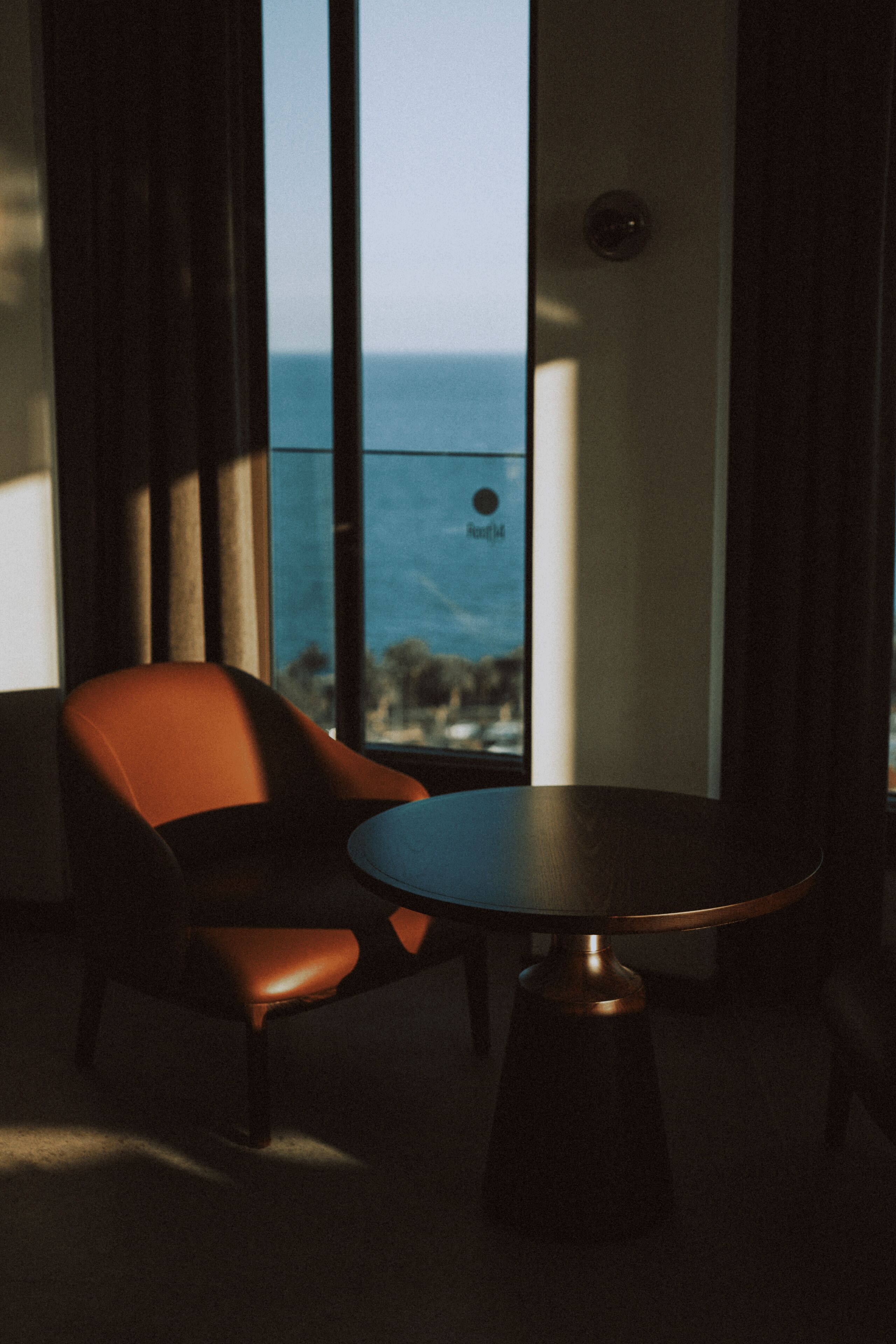 Una habitación con una sola silla y mesa, un ventanal con vista al mar y un picaporte visible.
