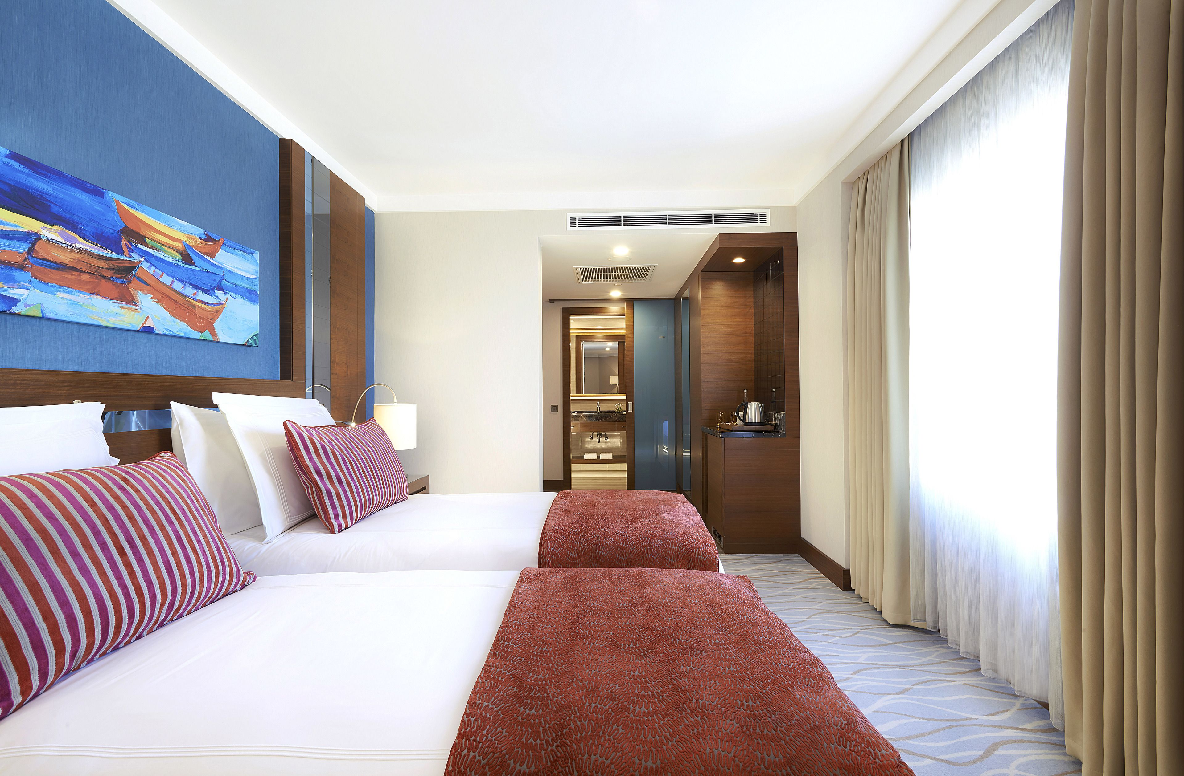 Habitación de hotel con dos camas, un cuadro en la pared, un escritorio y vistas al pasillo.