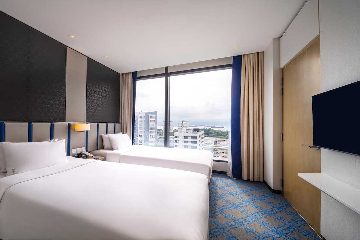 Een hotelkamer met twee bedden, een groot raam met uitzicht op de stad, een flatscreen televisie en een minibar.