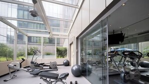 Un gimnasio moderno con diverso equipo de ejercicio, amplias ventanas y un muro de cristal que ofrece vistas al exterior.