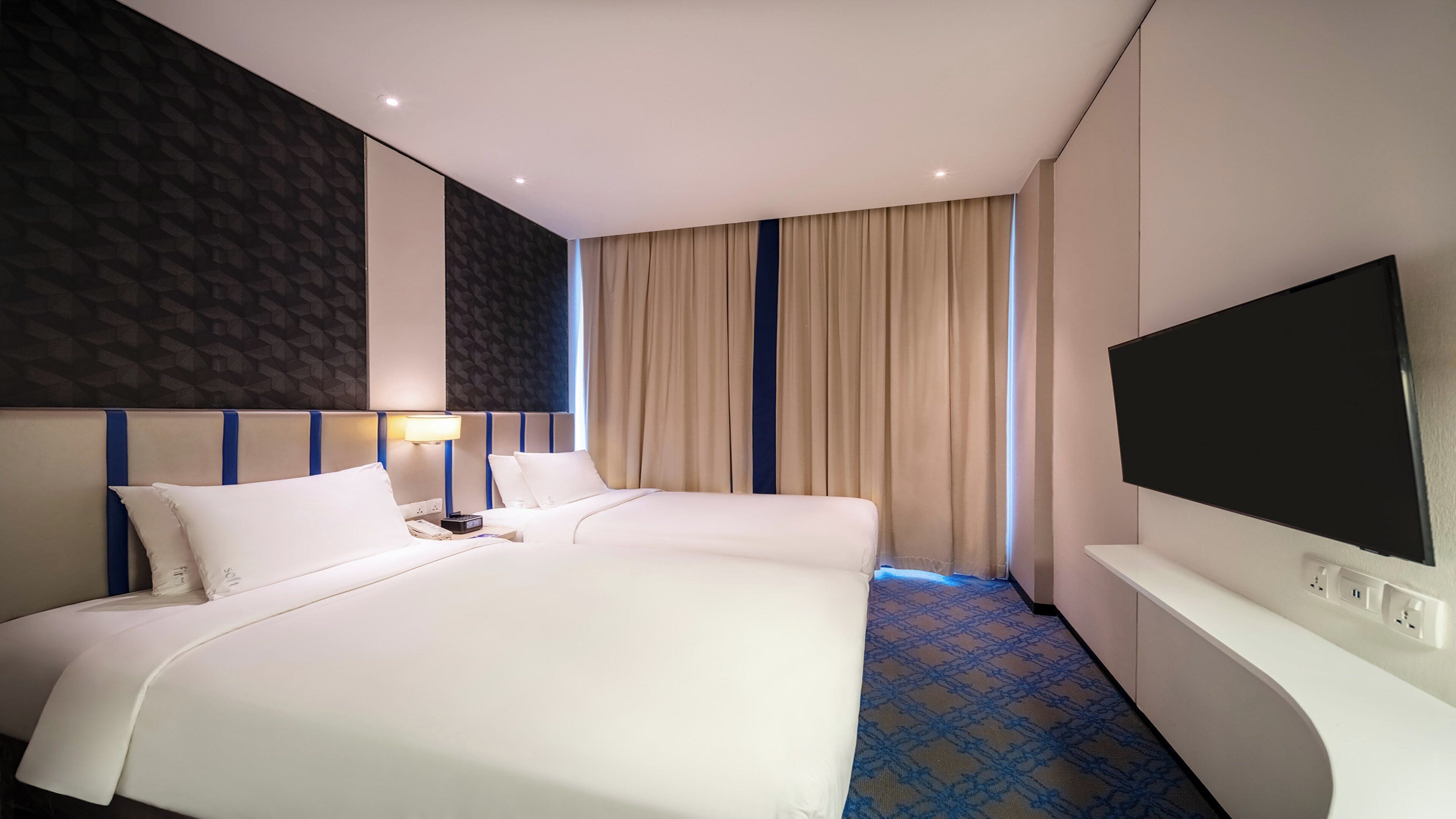 A hotel room with two beds, a TV, a lamp, and a patterned carpet.