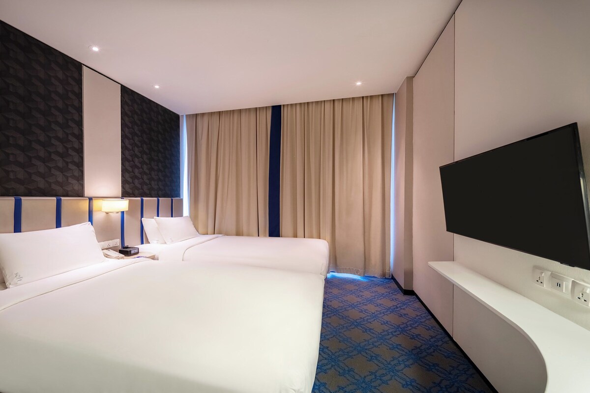 Ein Hotelzimmer mit zwei Betten, einem Fernseher, einer Lampe und einem gemusterten Teppich.