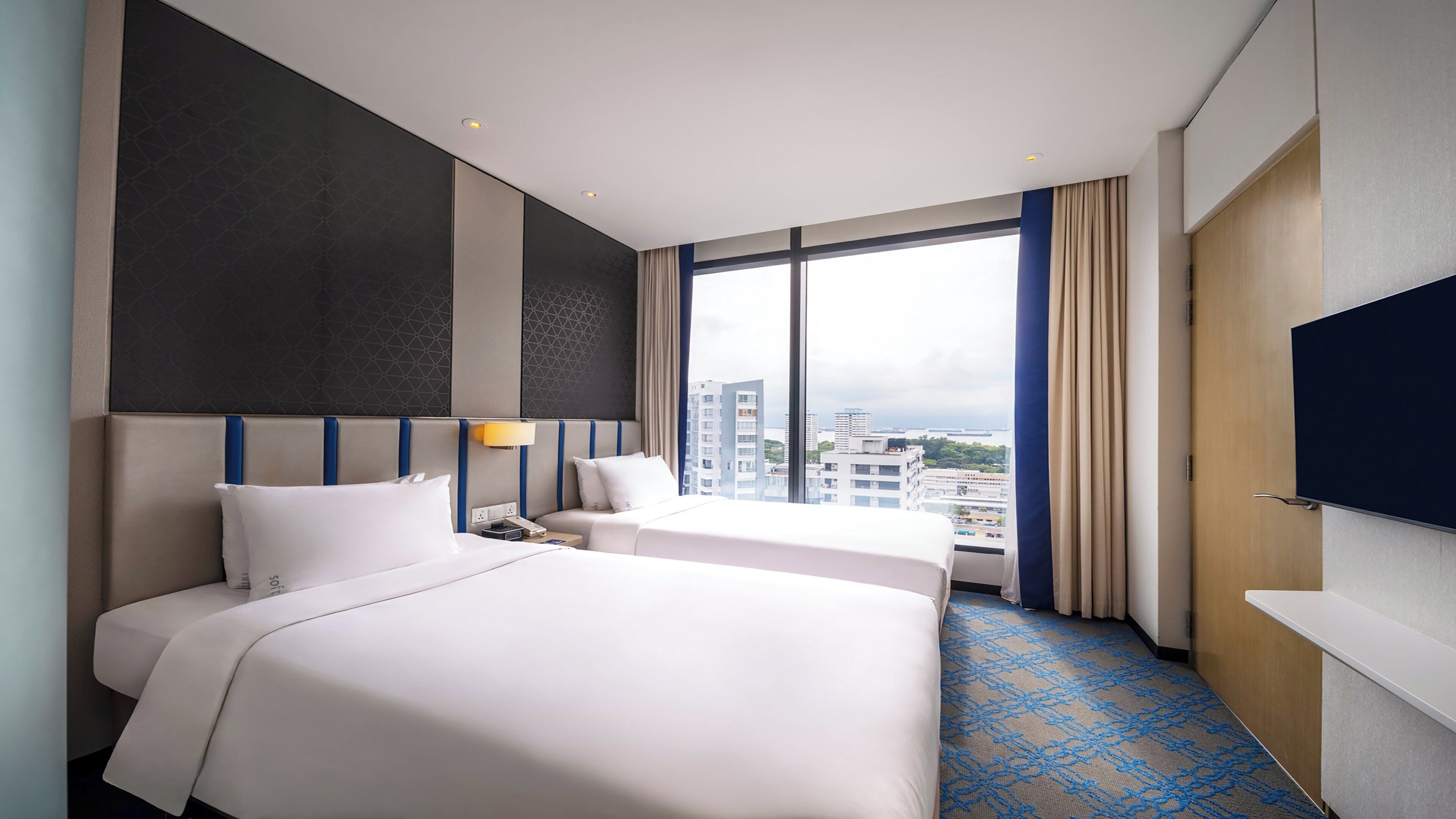 Une chambre d’hôtel avec deux lits, une grande fenêtre donnant sur la ville et un téléviseur à écran plat.