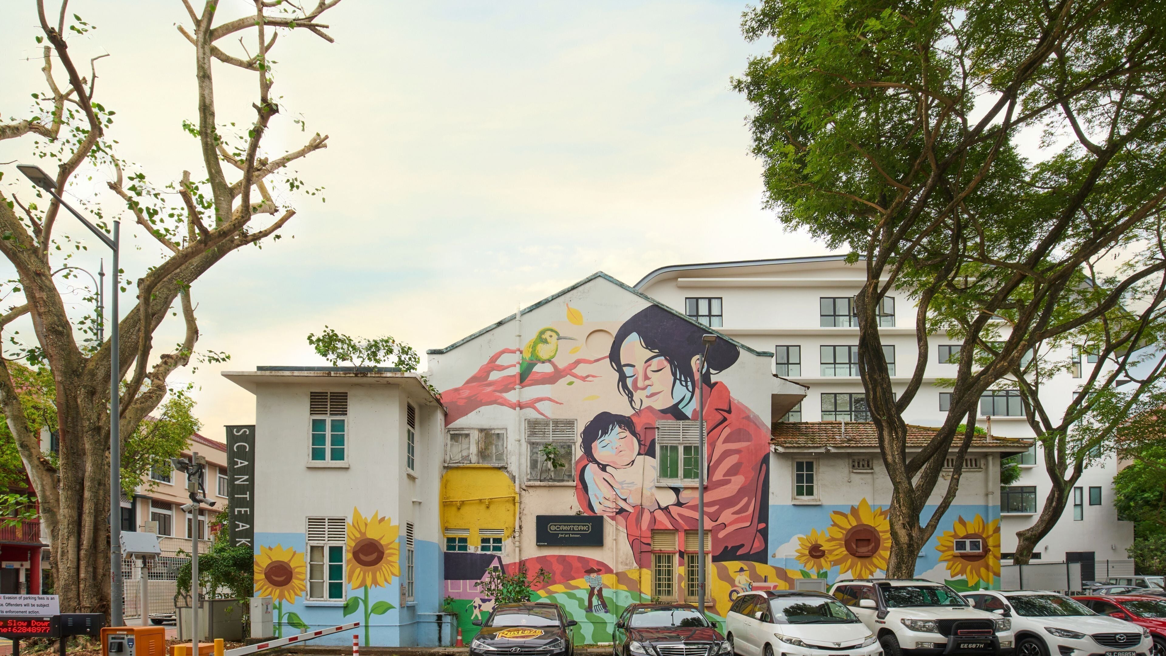 A building with a mural of a woman and child, surrounded by trees and parked cars.