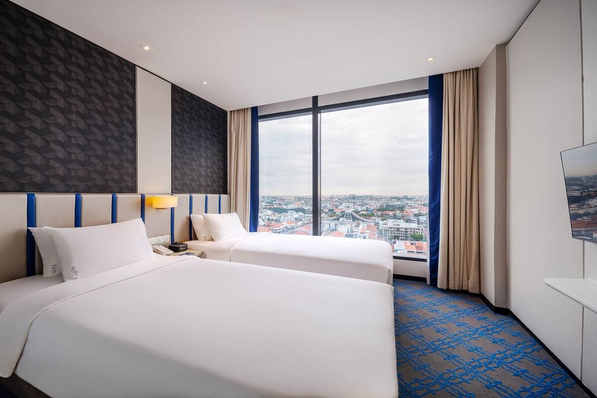 Hotelkamer met twee bedden, een groot raam met uitzicht op de stad, een flatscreen-tv en een kamerbreed tapijt met een patroon.