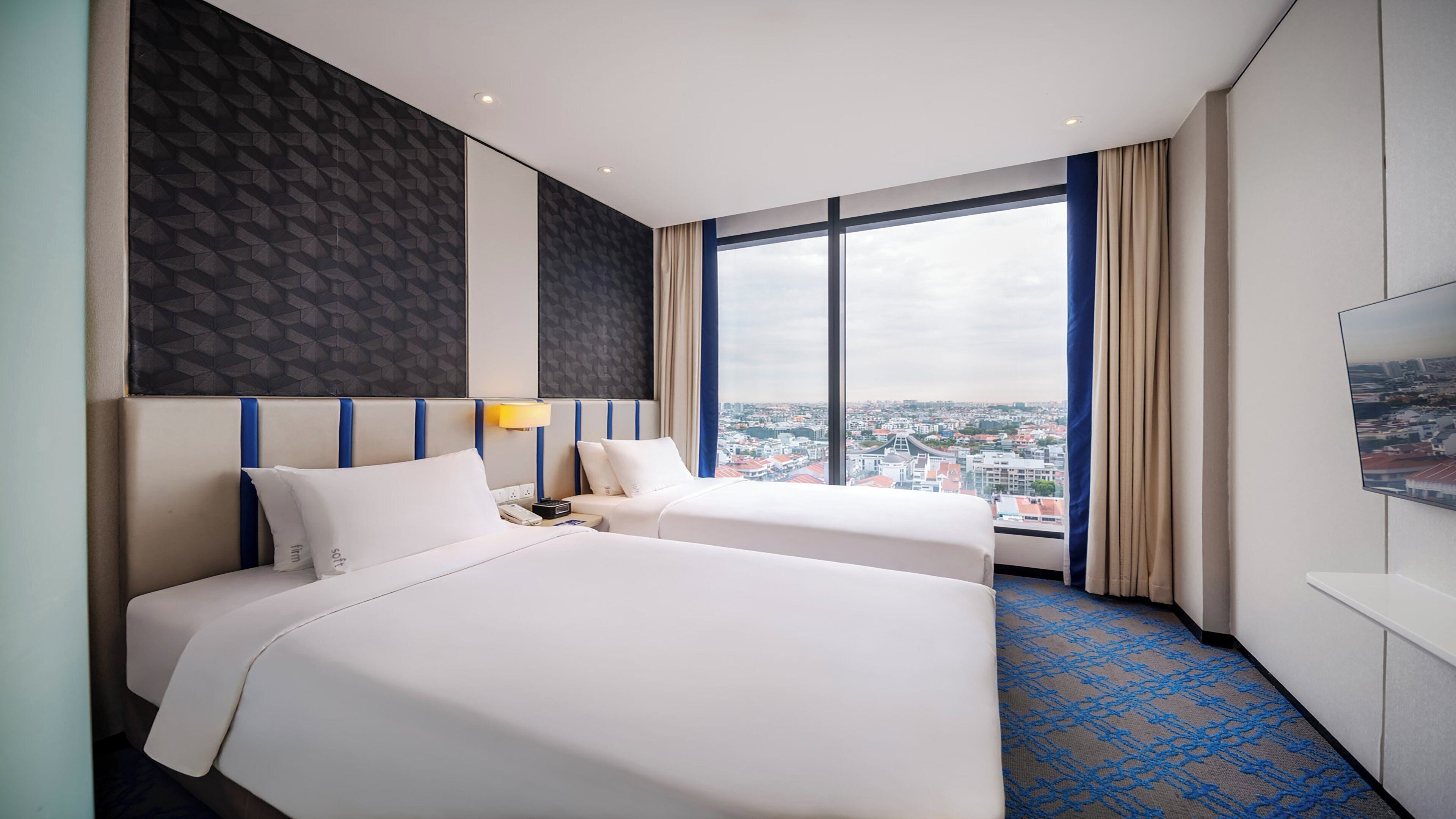 Een hotelkamer met twee bedden, een groot raam met uitzicht op de stad, een flatscreen televisie en een kamerbreed tapijt met een patroon.