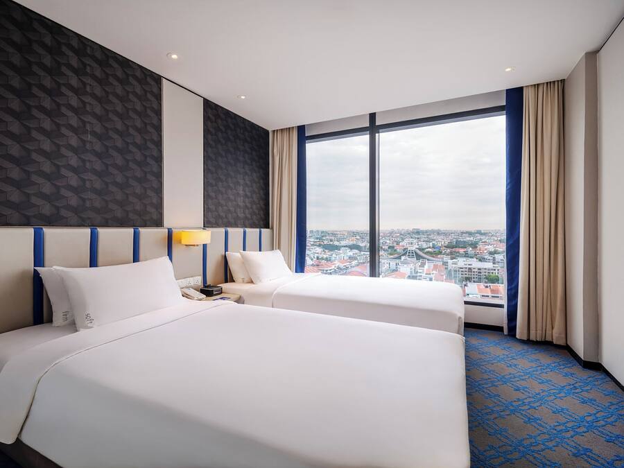 Een hotelkamer met twee bedden, een groot raam met uitzicht op de stad, een flatscreen televisie en een kamerbreed tapijt met een patroon.