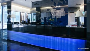Un mostrador de recepción moderno con una barra iluminada en azul, una pared con el texto 'Welcome' y 'Holiday Inn Express', y vista del área de recepción.