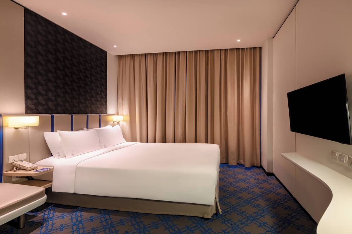 Een hotelkamer met een groot bed, een nachtkastje met een telefoon, een flatscreen televisie aan de muur en een kamerbreed tapijt met een patroon.