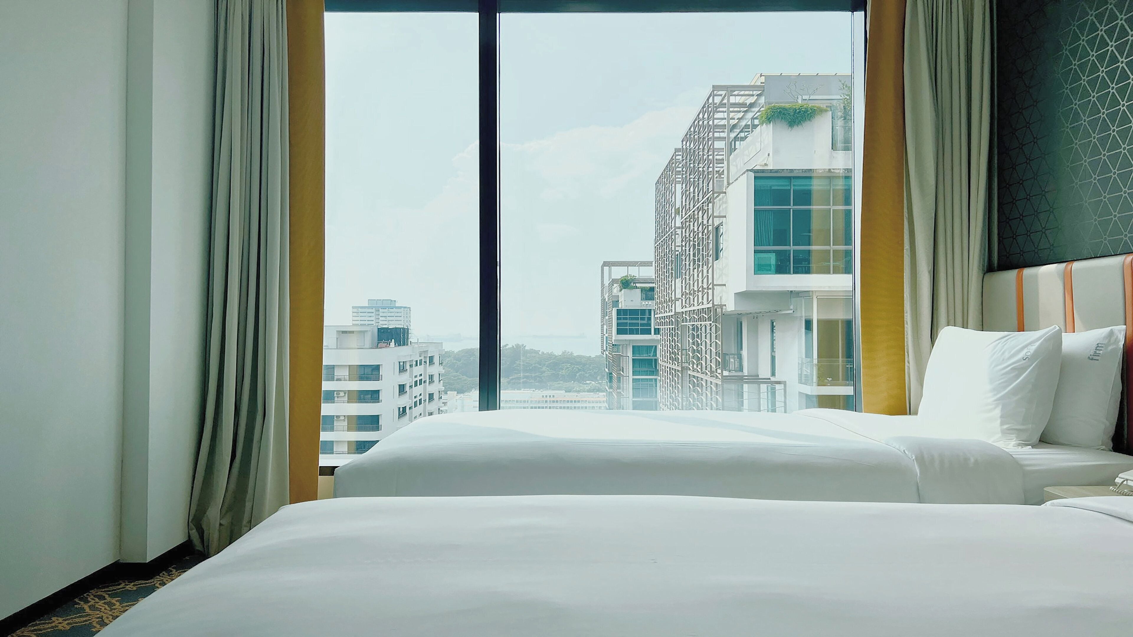 Une chambre d’hôtel avec une grande fenêtre, un lit et une vue sur des immeubles modernes.