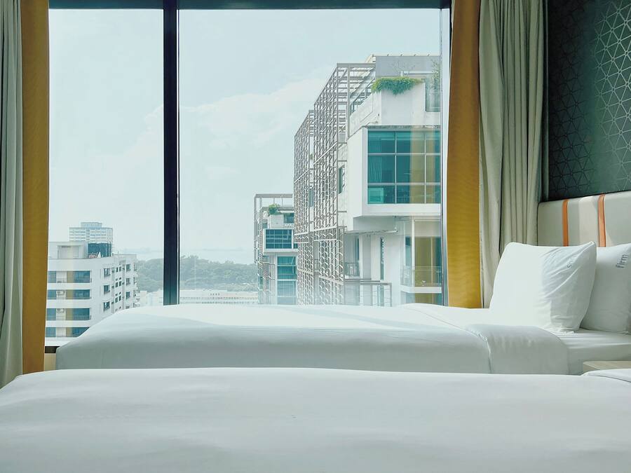 Une chambre d’hôtel avec une grande fenêtre, un lit et une vue sur des immeubles modernes.