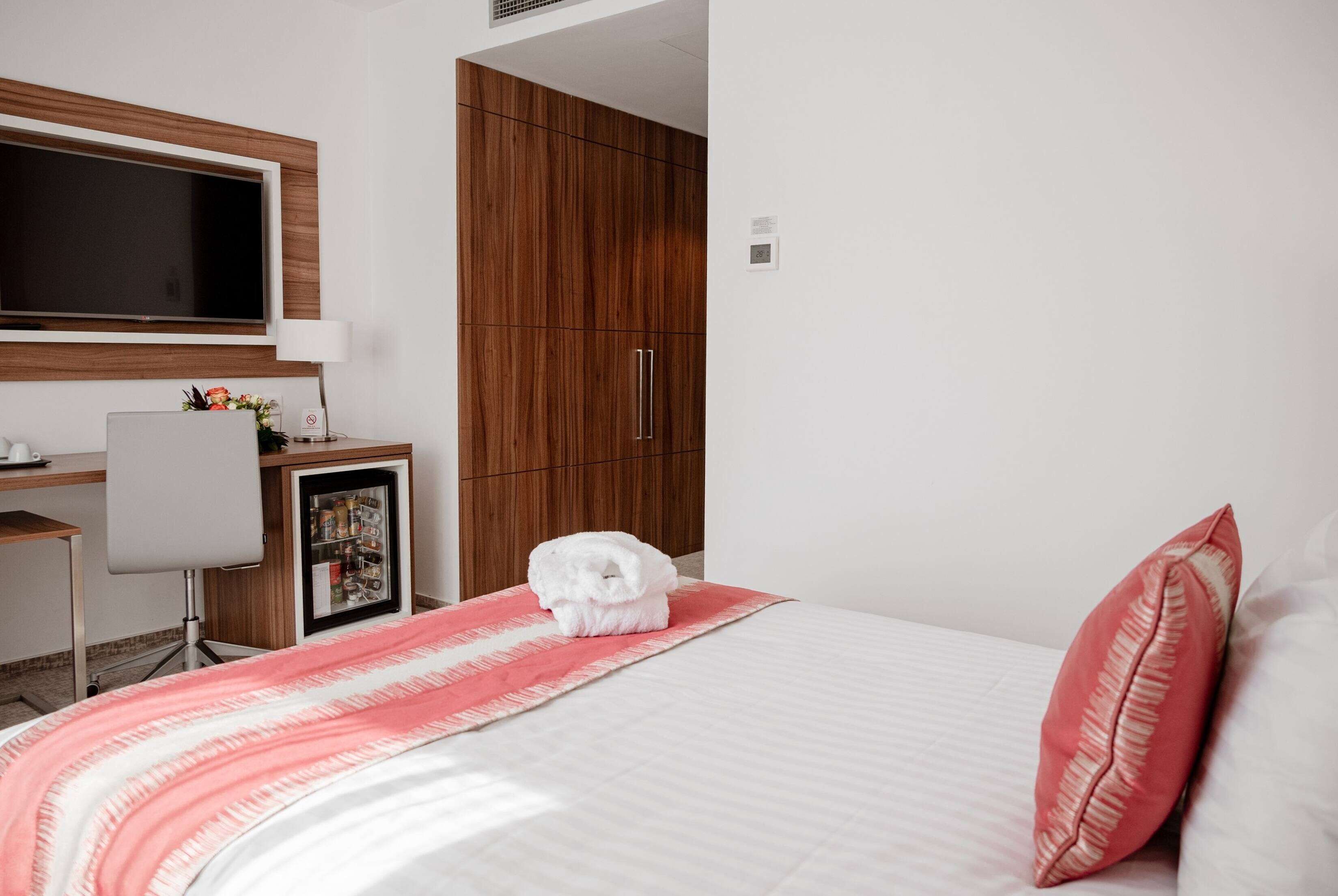 A hotel room with a bed, a desk with a chair, a TV, and a wardrobe.
