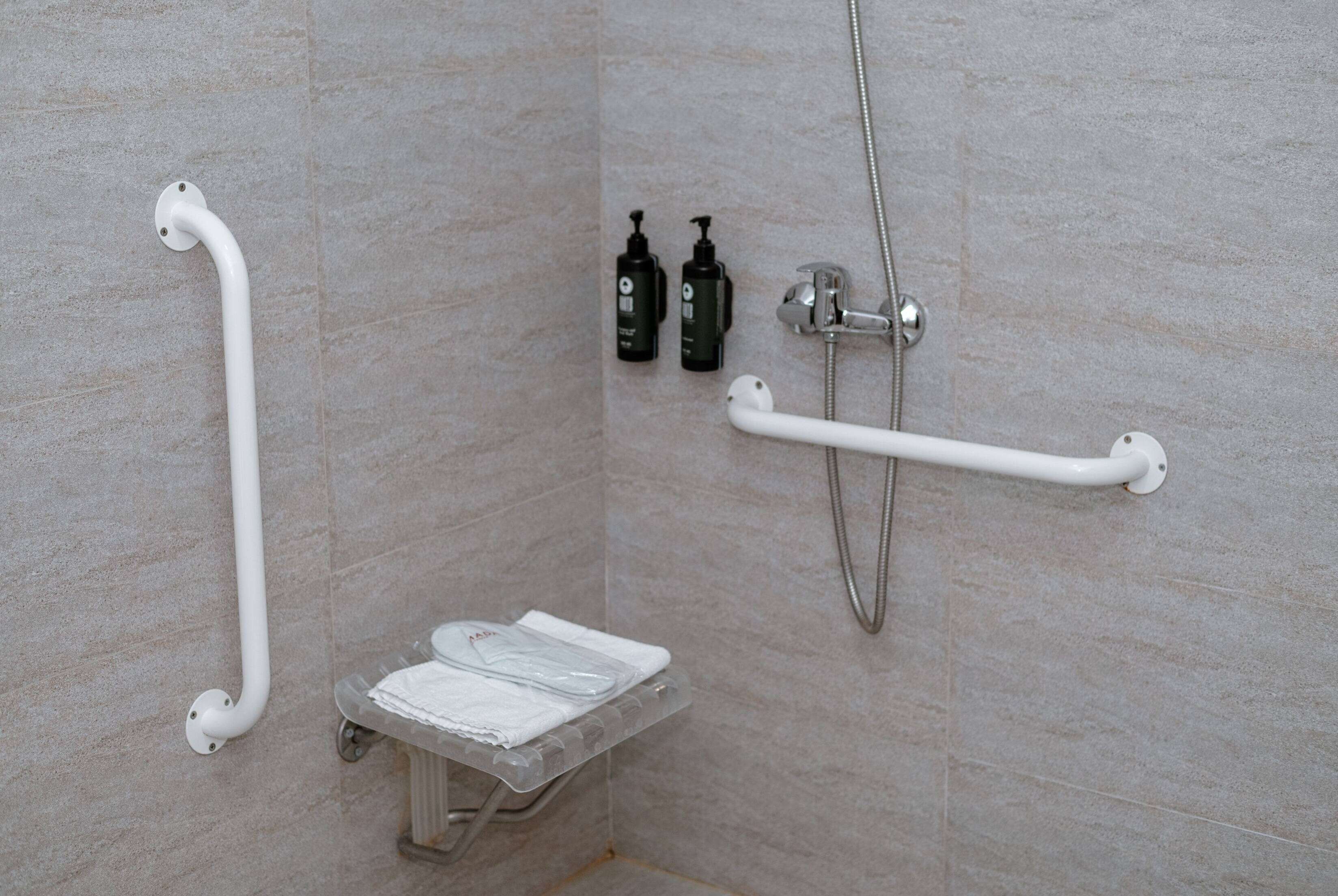 A bathroom with a shower, grab bars, a small bench, and two bottles of shampoo.