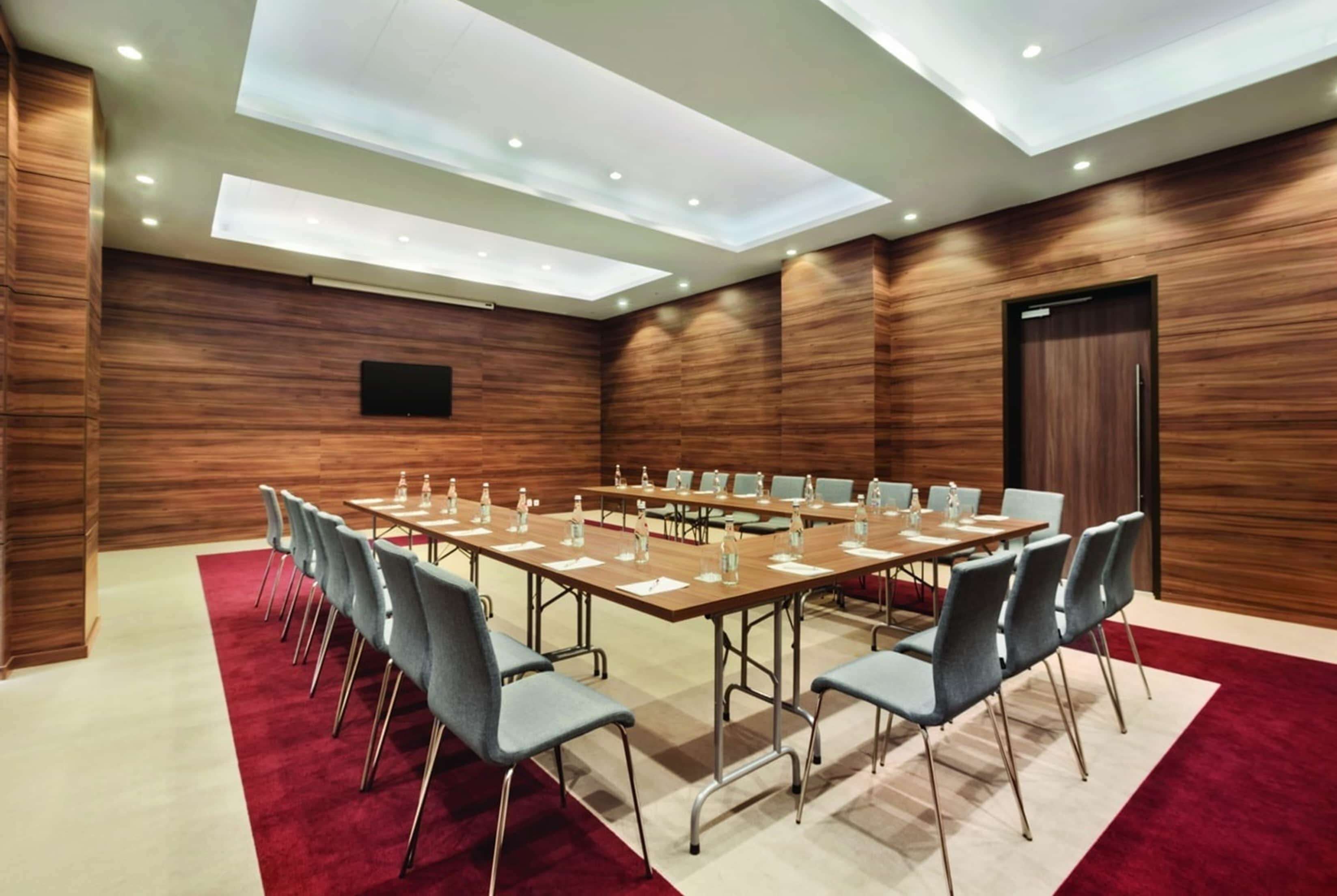 Un salón de conferencias con una larga mesa, sillas y una alfombra roja.