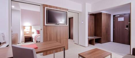 Una habitación de hotel moderna con un escritorio de madera, un televisor montado en la pared, una cama con una mesita de noche y un armario.