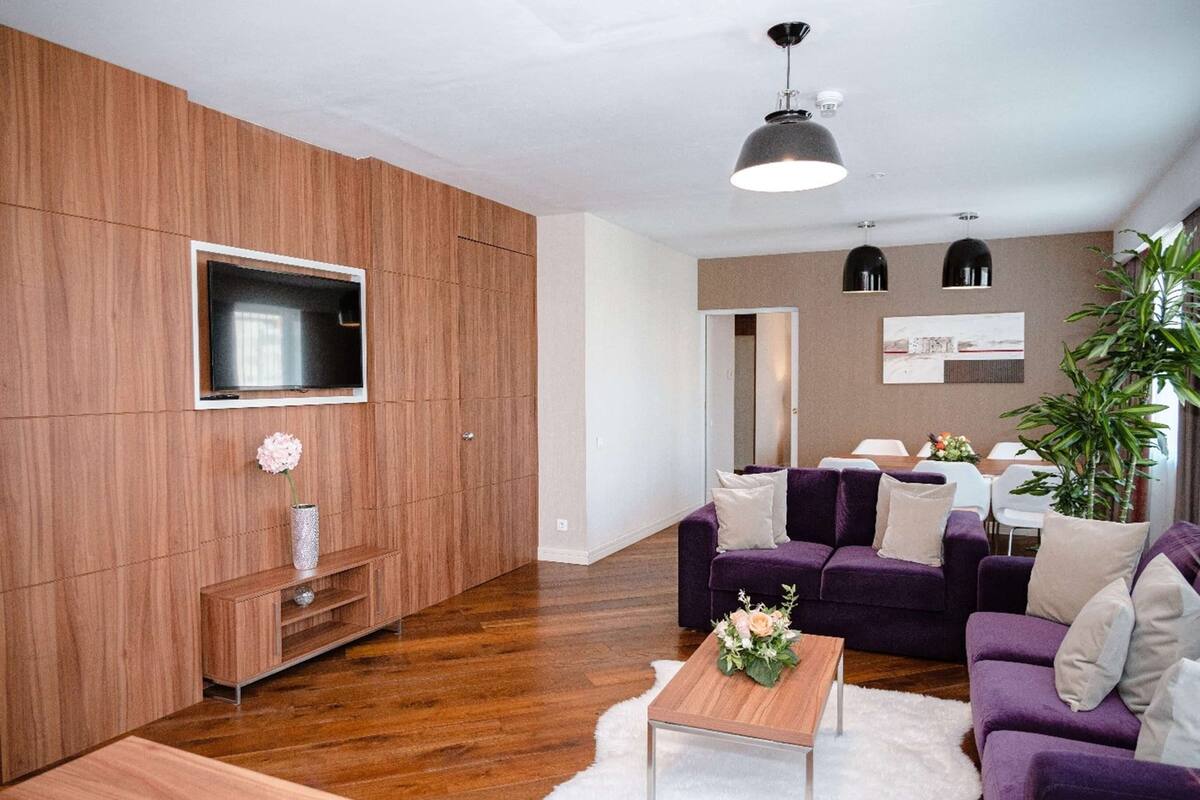Una sala de estar moderna con una pared de acento de madera, un televisor de pantalla plana, un juego de sofá color púrpura y una mesa de centro.